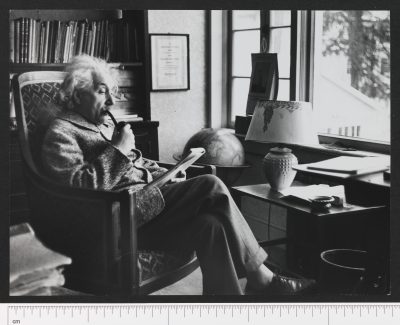 Aufnahme des Wissenschaftlers Albert Einstein von Eric Schaal. Einstein sitzt lesend und Pfeife rauchend in einem Sessel.