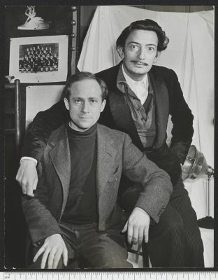 Aufnahme von Eric Schaal gemeinsam mit dem Surrealisten Salvador Dalí. Schaal sitzt auf einem Stuhl, Dalí seitlich dahinter auf der Stuhllehne.