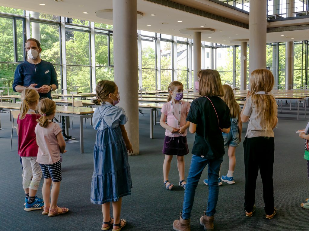 Gruppe von 7 Kindern und einem Erwachsenem im Arbeitsbereich des Hauptlesesaals der DNB Frankfurt.