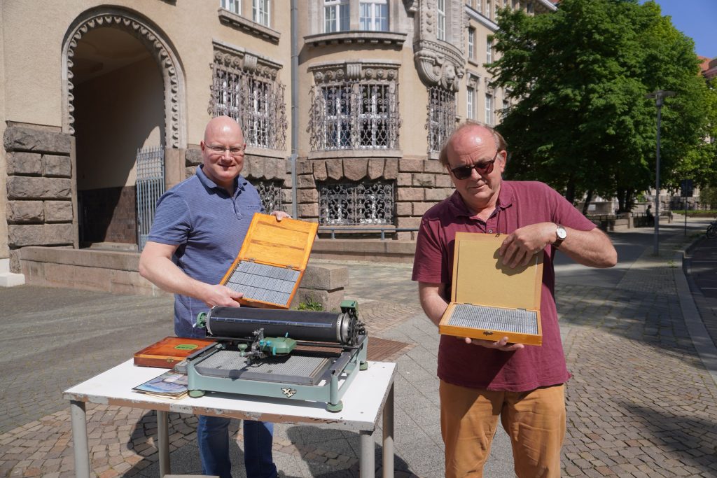 Beide Männer stehen mit der Schreibmaschine vor der Deutschen Nationalbibliothek.