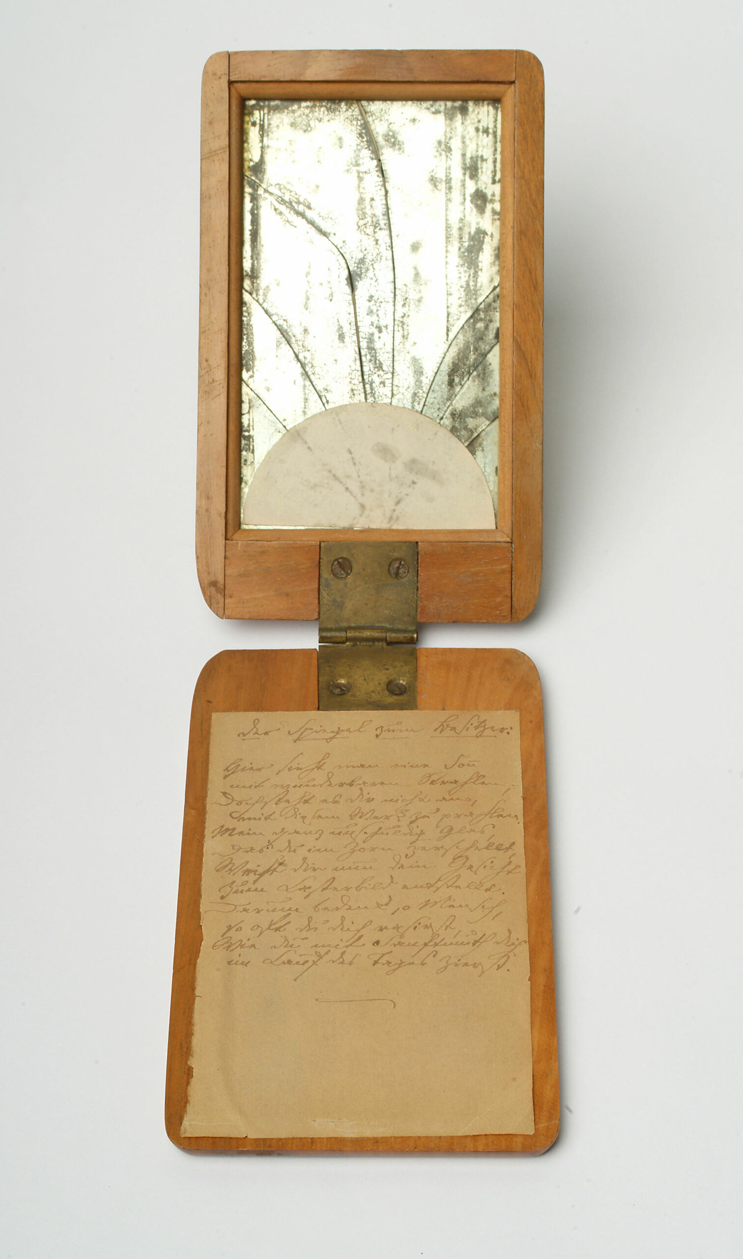 Abbildung eines aufklappbaren Spiegels auf Holzplatten, auf der Platte ohne Spiegel ist ein Text auf Papier befestigt