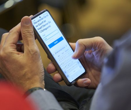 Eine Hand hält ein Smartphone, auf dem die Frage steht: Was verbinden Sie mit der Zukunft der Arbeit?