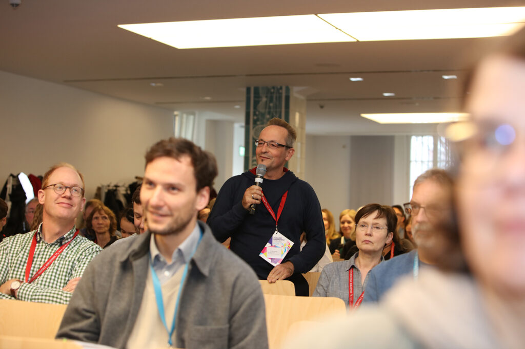 Ein Mann aus dem Publikum steht und redet ins Mikrofon