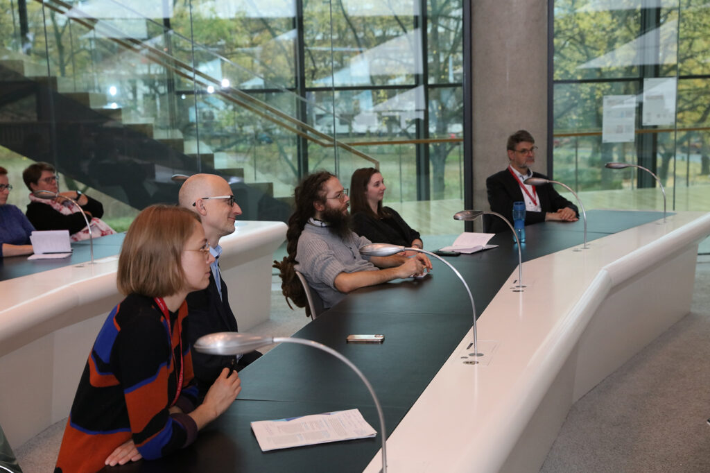 Mehrere Menschen sitzen in einem modernen Lesesaal und sehen interessiert nach vorne