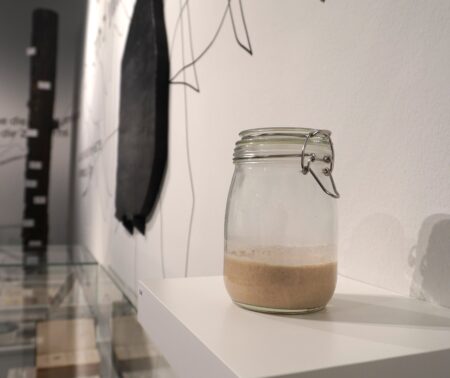 Einmachglas zu einem Drittel gefüllt mit braunem Sauerteig steht in einer Ausstellung.