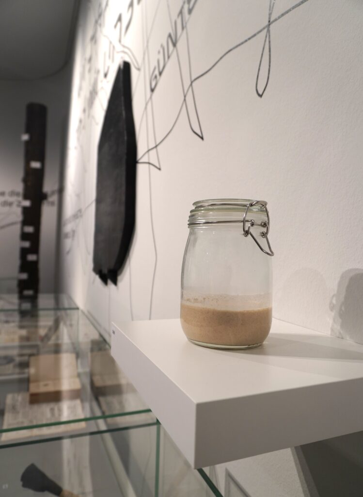 Einmachglas zu einem Drittel gefüllt mit braunem Sauerteig steht in einer Ausstellung.
