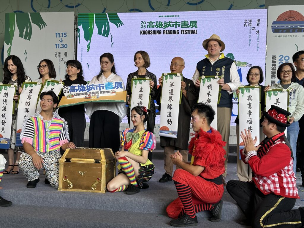 Gruppenfoto auf einer Bühne beim Kaohsiung Reading Festival: Menschen halten Banner mit chinesischer Schrift, davor Performer in bunten Kostümen.