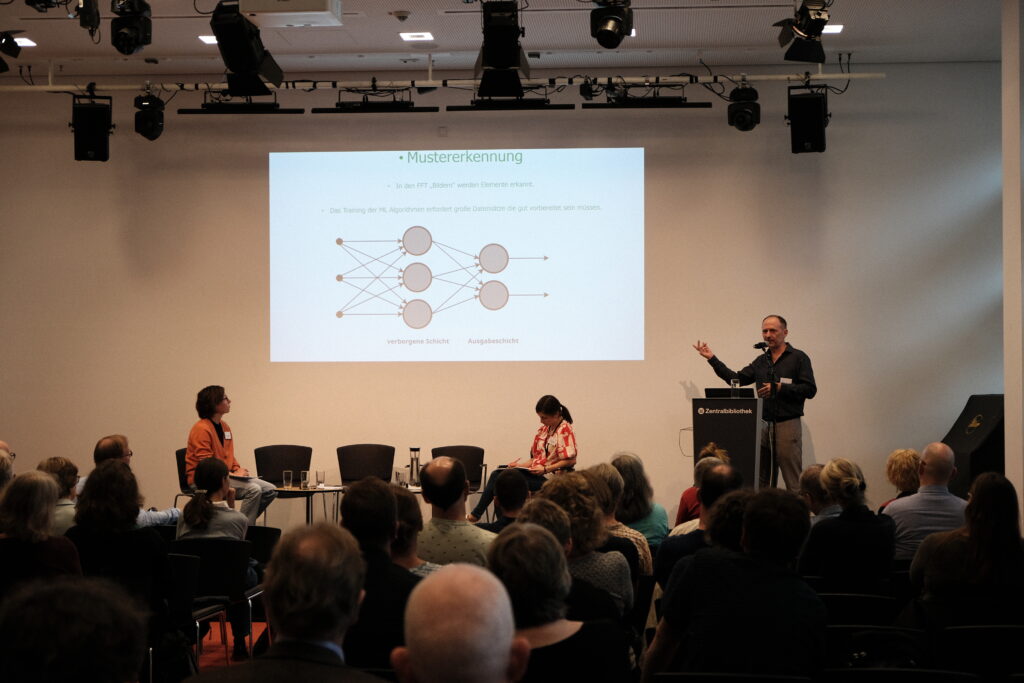 Viele Menschen sitzen im Publikum und hören jemandem zu, der einen Vortrag hält.