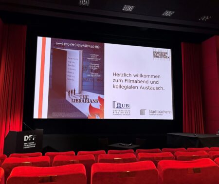 Blick über die Kinosessel auf die Leinwand mit dem Filmplakat und der Begrüßung des Publikums