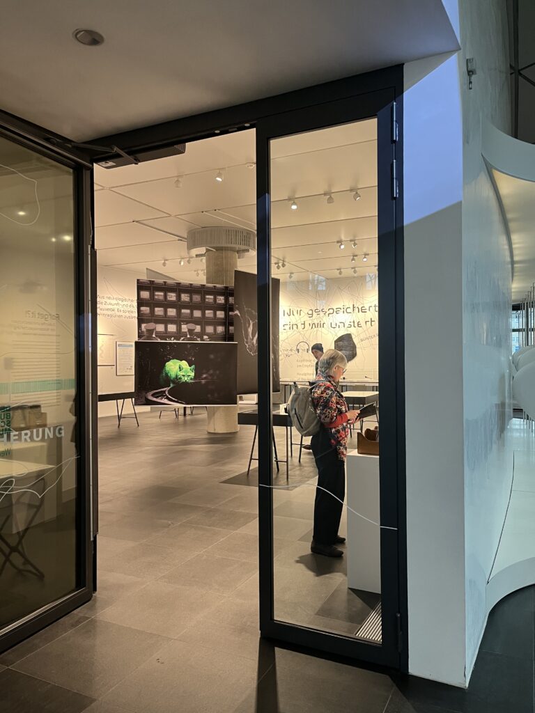 Geöffnete Tür zu einer Ausstellung. Darin zu sehen ist ein Plakat mit einer neongrünen Katze.