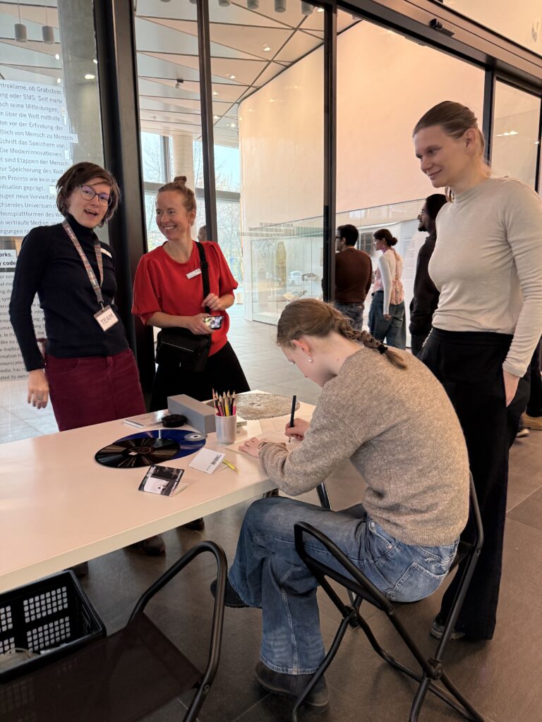 Mehrere Menschen stehen um einen Tisch, eine Person schreibt etwas