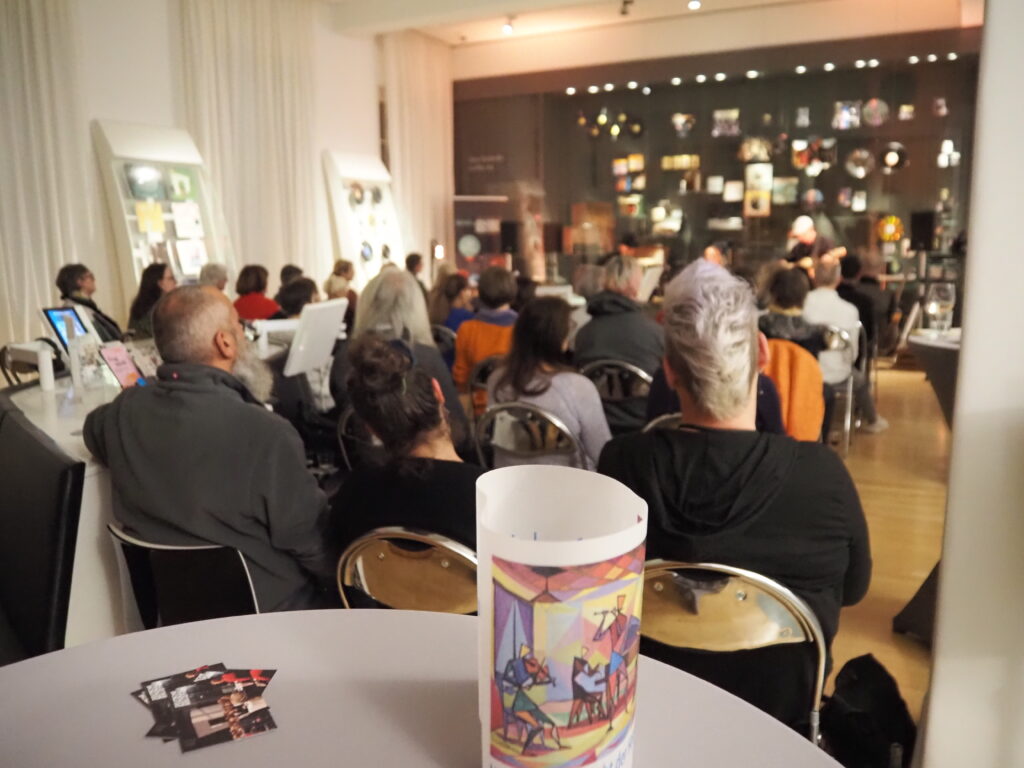 Viele Zuhörer sitzen in mehreren Reihen vor der Band.