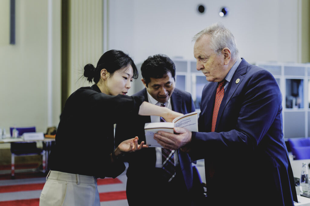 Drei Kongressteilnehmer schauen gemeinsam in ein Buch. Eine junge Frau deutet auf das Buch und erklärt.