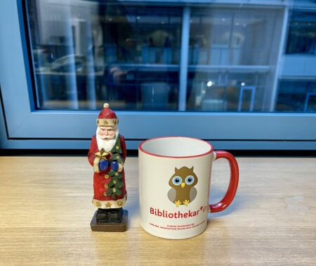 Ein Weihnachtsmann aus Holz und eine Tasse mit der Aufschrift Bibliothekar*in und eine Eule