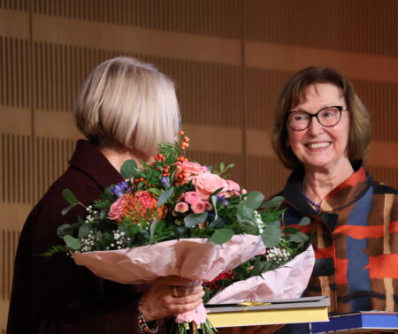 Zwei Personen sind zugewandt, lächeln, halten Blumen in der Hand
