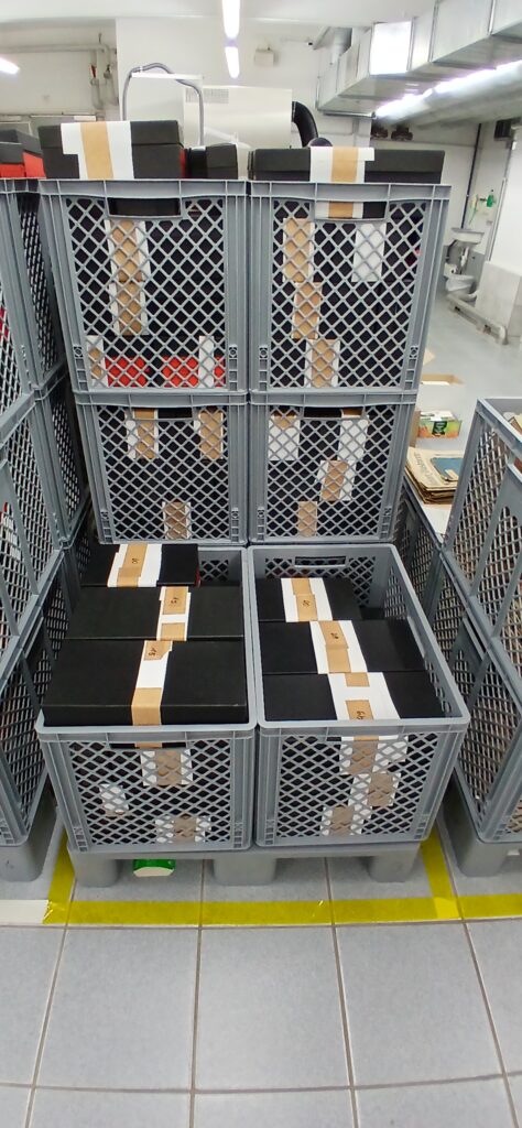 Mehrere schwarze Boxen stehen in grauen Kisten
