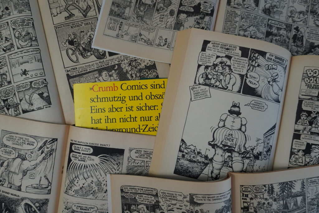 Aufgeschlagene Comic-Hefte. In der Mitte liegt ein gelber Zettel im Anschnitt. Darauf zu lesen "Crumb Comics sind schmutzig und obszön"