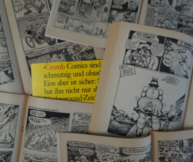 Aufgeschlagene Comic-Hefte. In der Mitte liegt ein gelber Zettel im Anschnitt. Darauf zu lesen "Crumb Comics sind schmutzig und obszön"