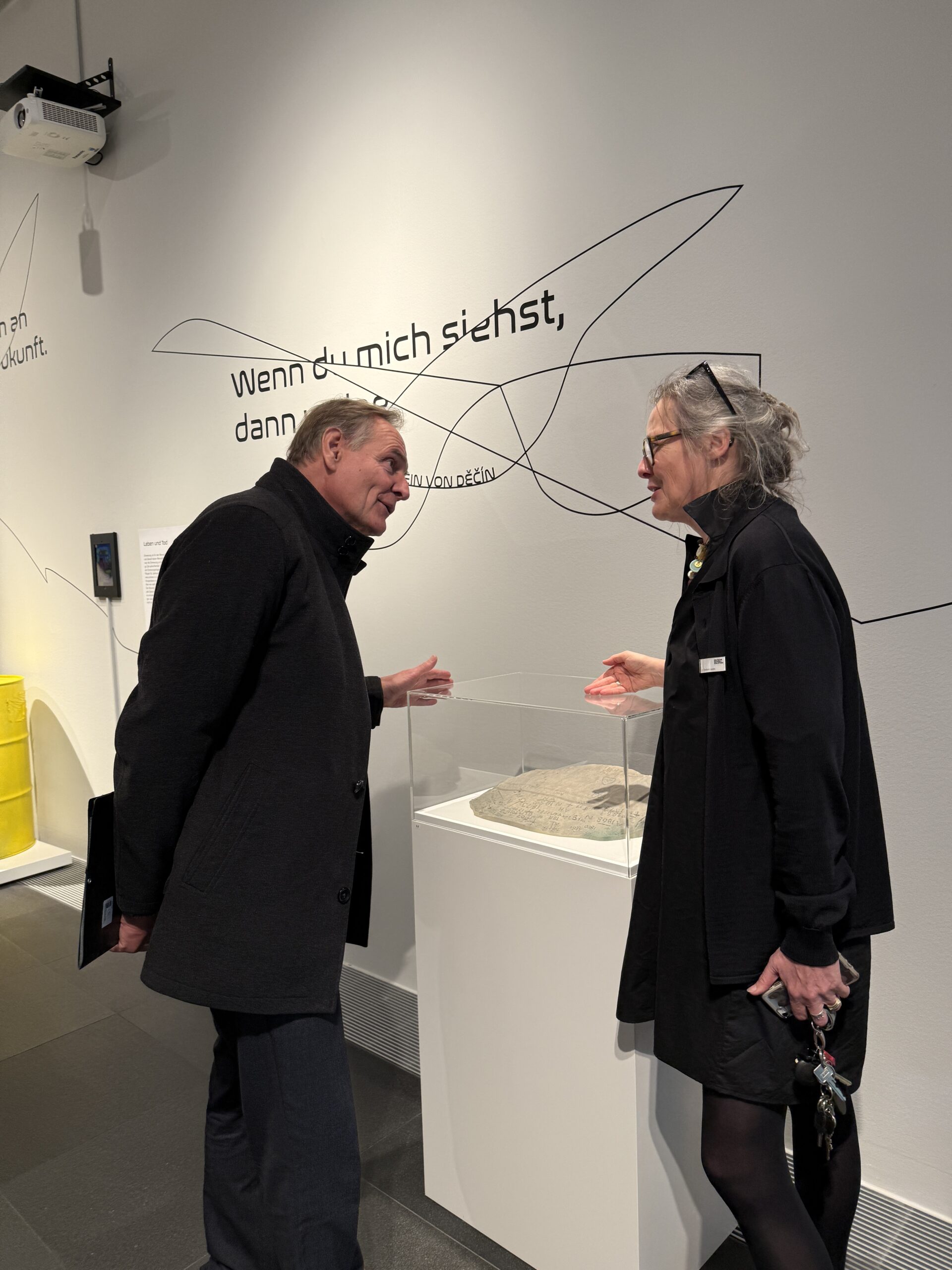 Zwei Menschen unterhalten sich angeregt neben einer Ausstellungsvitrine.