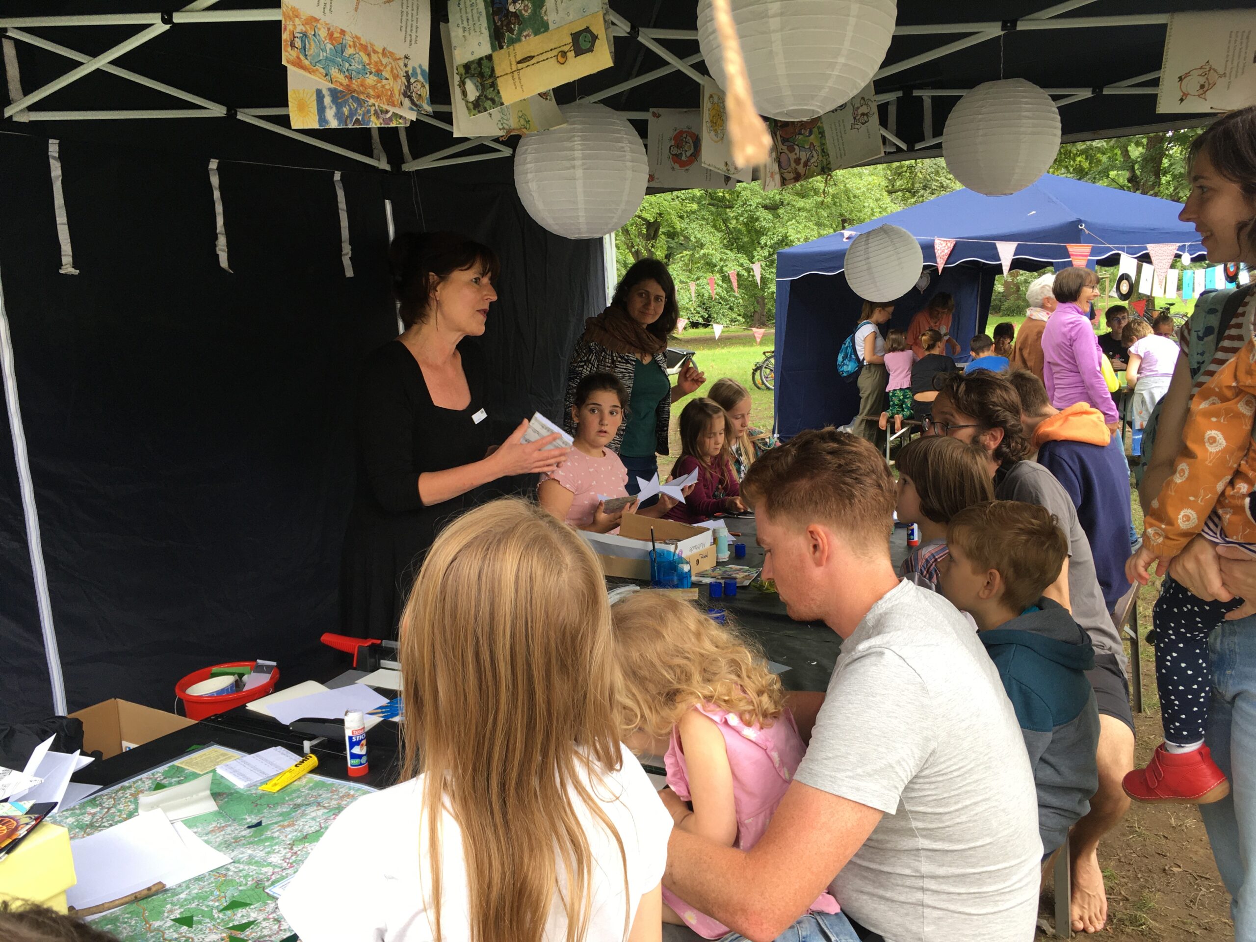 Eine Frau erklärt einer Gruppe Kinder und Erwachsener einfache Falt- und Buchbinde-Techniken.