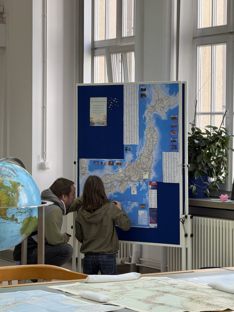Eine große Karte hängt auf einer Metaplanwand. Davor stehen zwei Menschen und schauen sich die Karte von Japan an.