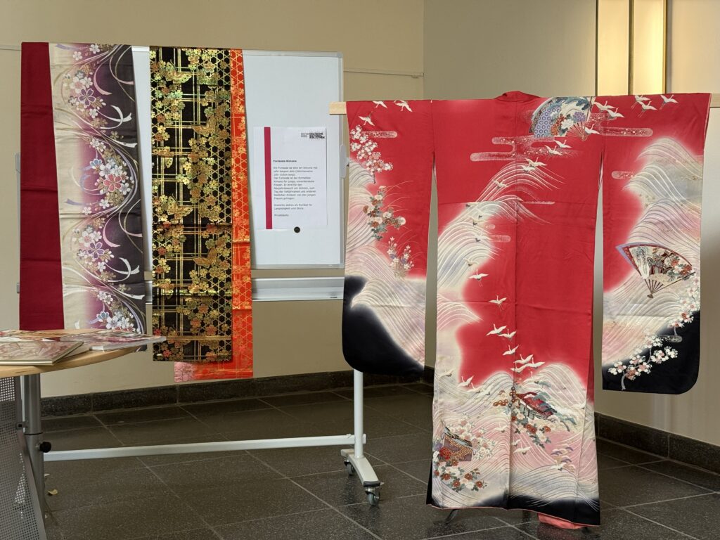 Ein rosa Kimono mit langen Ärmeln hängt da mit zwei farbenprächtigen breiten Gürteln