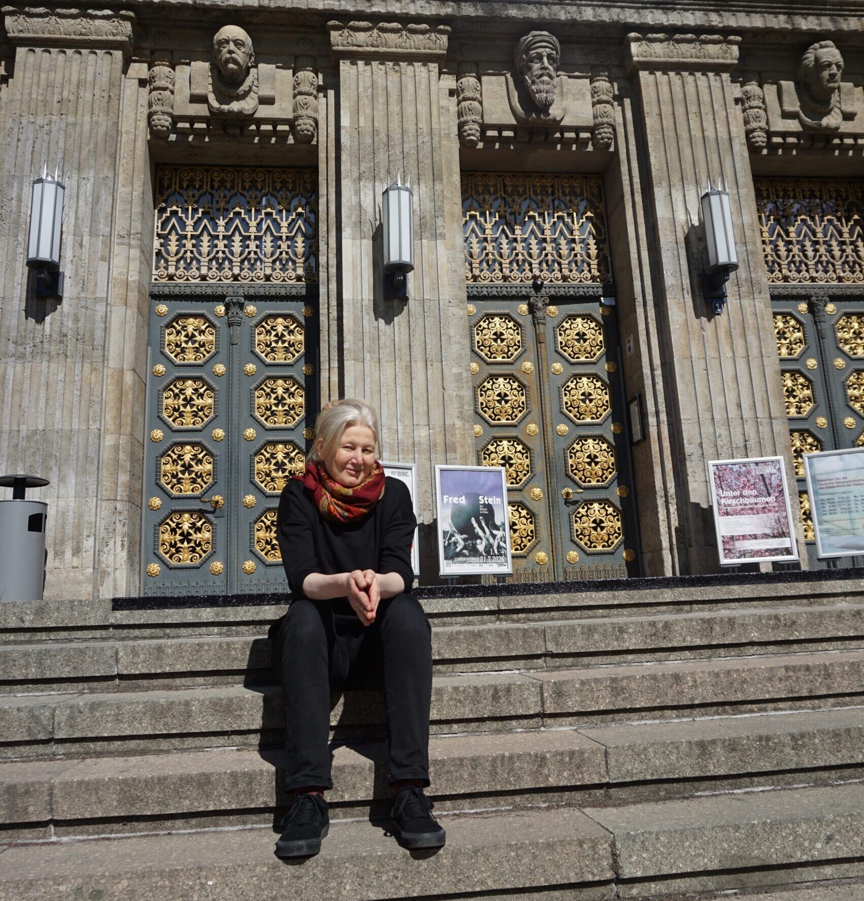 Es zeigt Gerda Raidt, wie sie auf den Eingangstreppen zur Bibliothek sitzt.