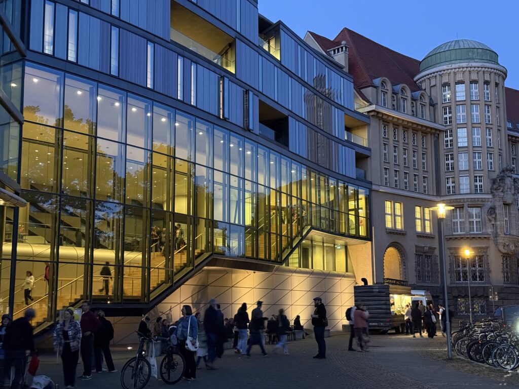 Außenanblick der gläsernen Fassade des Museums und Teilen des historischen Gebäudes. Es ist dämmriges Licht.