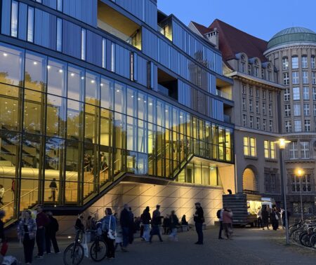 Außenanblick der gläsernen Fassade des Museums und Teilen des historischen Gebäudes. Es ist dämmriges Licht.