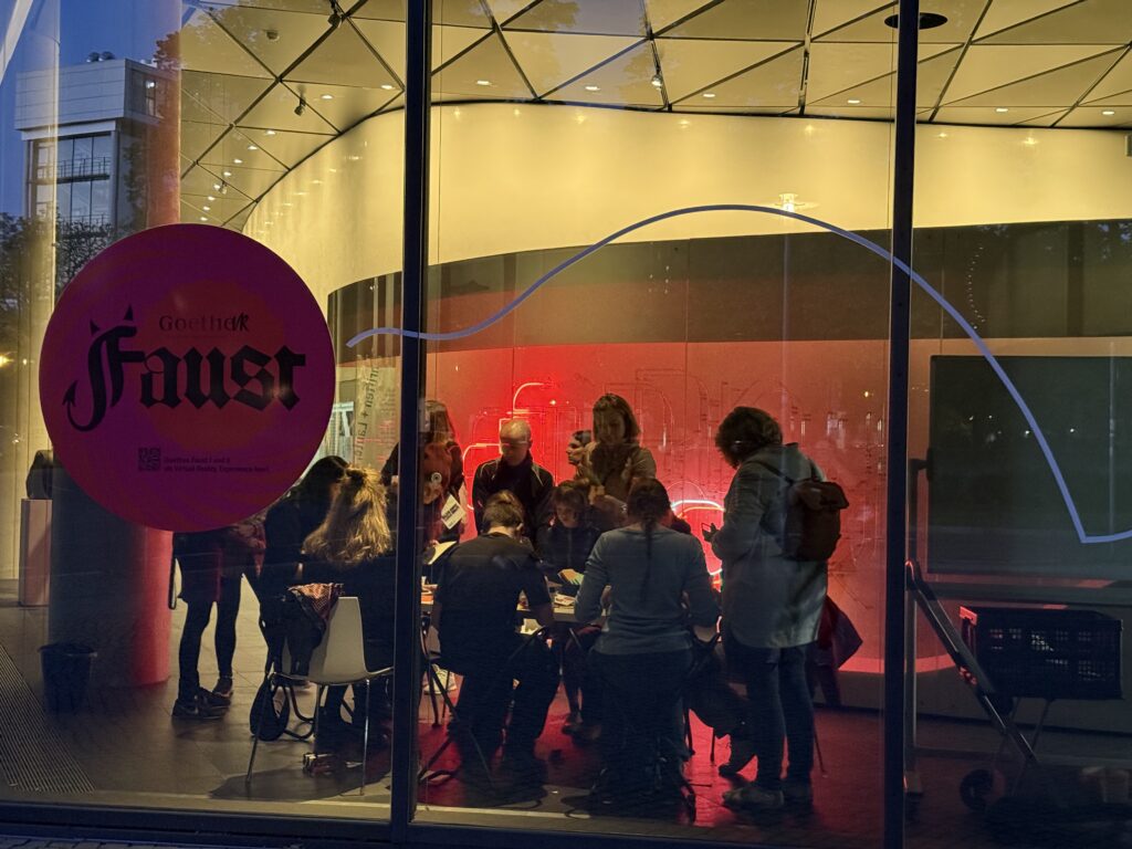 Blick von außen durch eine Glasscheibe in ein Museum. Menschen sitzen innen an einem Tisch.
