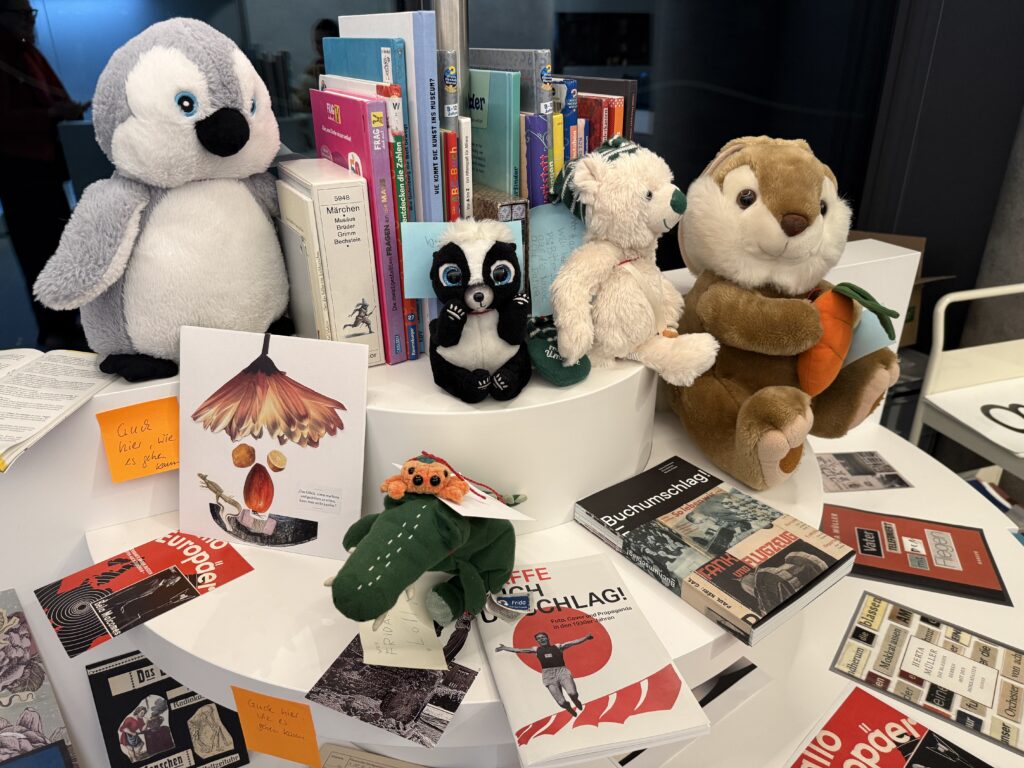 Einige Kuscheltiere sitzen in der Leseecke und schauen sich Bücher und Collagen an