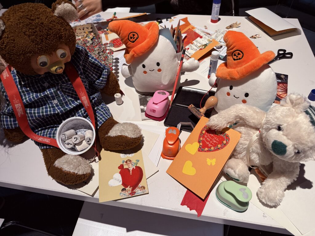 Zwei Kuscheltier-Geister und zwei Bären basteln Karten aus Papier für den Muttertag.
