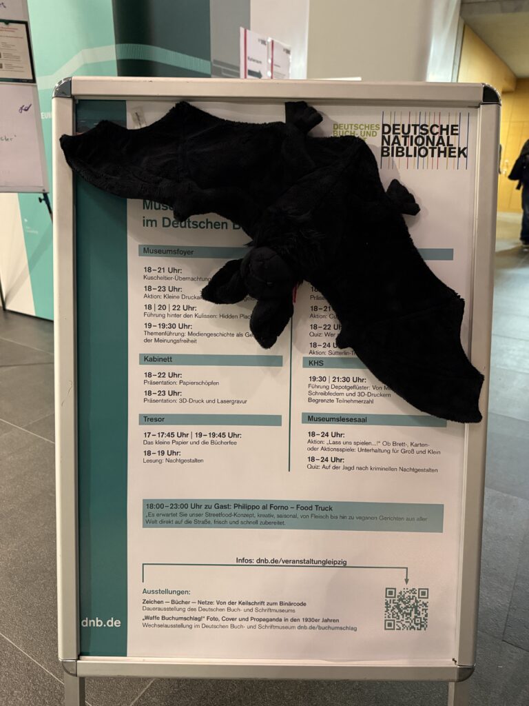 Eine Kuscheltier-Fledermaus hat sich an den Plakataufsteller gehangen.
