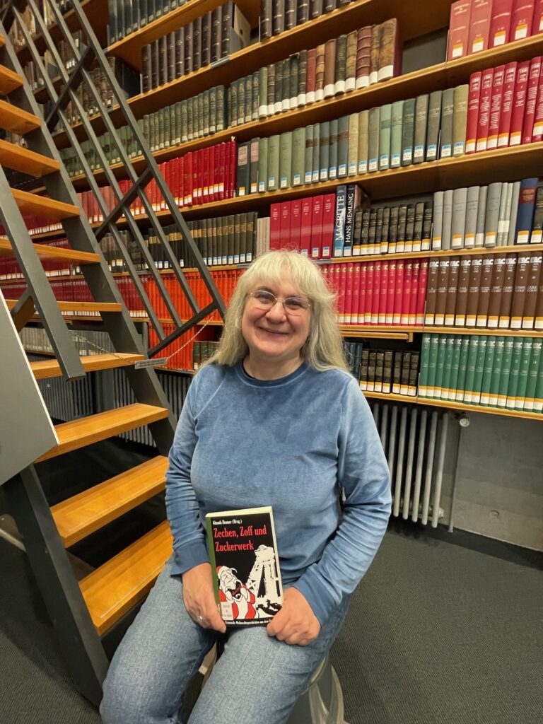Die Autorin Almuth Heuner sitzt auf einer Treppe im Lesesaal der DNB Frankfurt mit ihrem Buch in der Hand