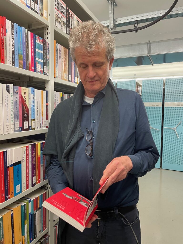 Matthias Arning mit einem Buch vor Regalen im Büchermagazin