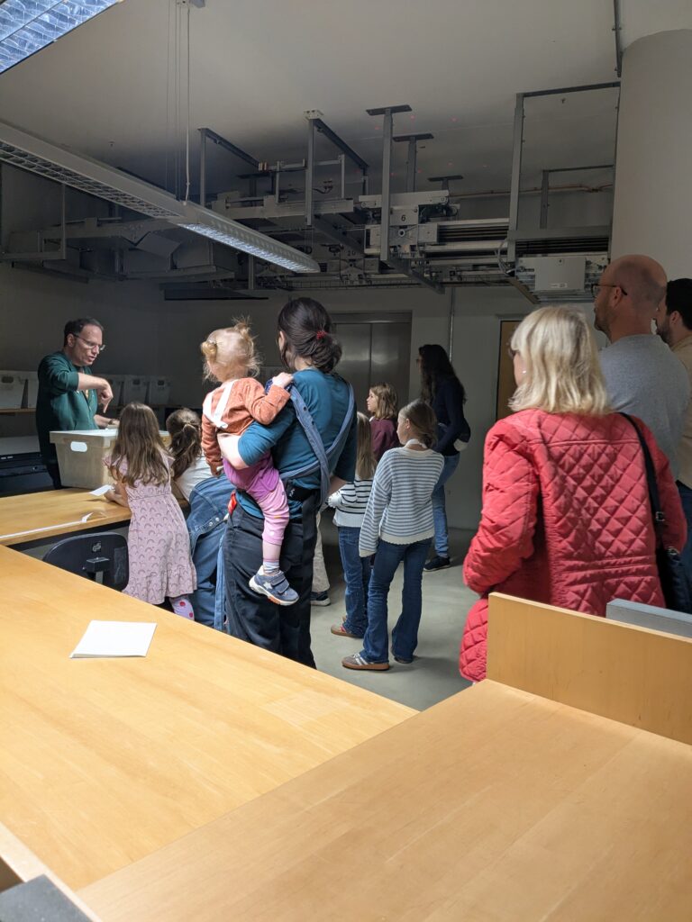 Kinder und Erwachsene stehen in einem Raum mit einer Buchtransportanlage.