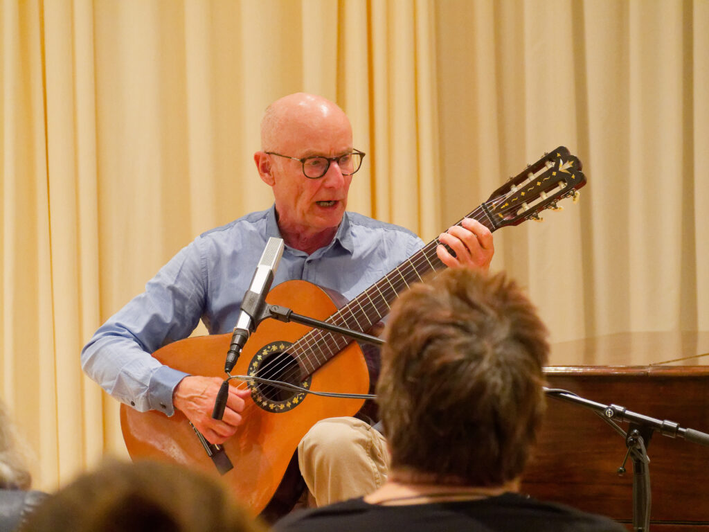 Ekkehrd Maaß spielt Gitarre und singt vor Publikum.