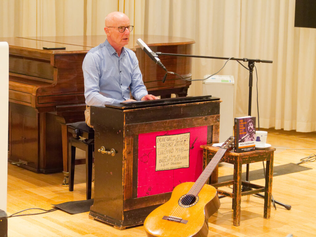 Ekke Maaß im Vortragsraum des Deutschen Musikarchive am Harmonium. Vor ihm liegen seine Gitarre und ein Buch zu Wolf Biermann.