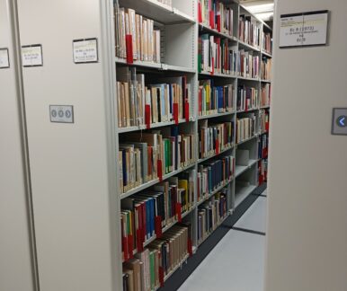 Zahlreiche Bücher füllen eine lange Regalreihe eines beweglichen Magazinschrankes. Man erkennt die hydraulischen Arme am oberen Bildrand.